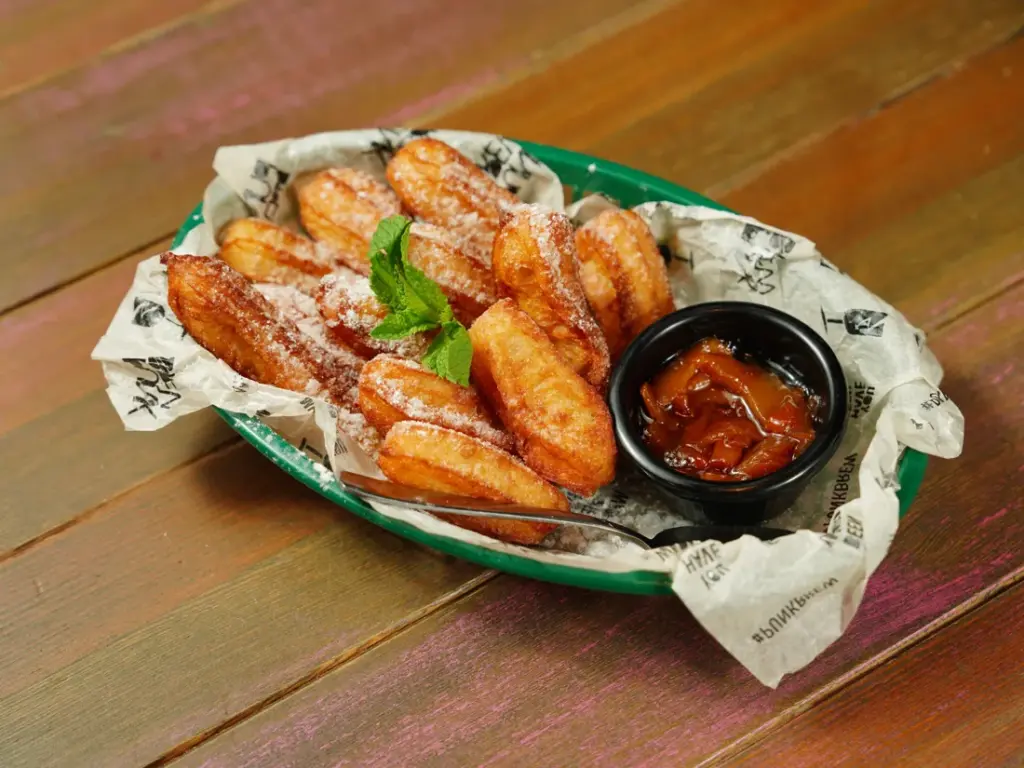 Panier de churros dorés saupoudrés de sucre, servis avec une petite coupelle de sauce